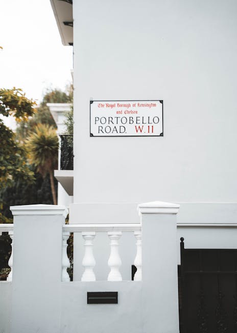A pair of rectangular red metal signs are mounted on a dark green metal post, with one slightly overlapping the other. The signs feature white text and logos, indicating a designated 'Alcohol Free Zon