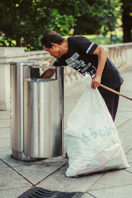 A small, three-wheeled cart is loaded with various types of waste and rubbish, including large cardboard boxes, plastic trash bags, and miscellaneous debris. The cart's metal frame appears weathered,